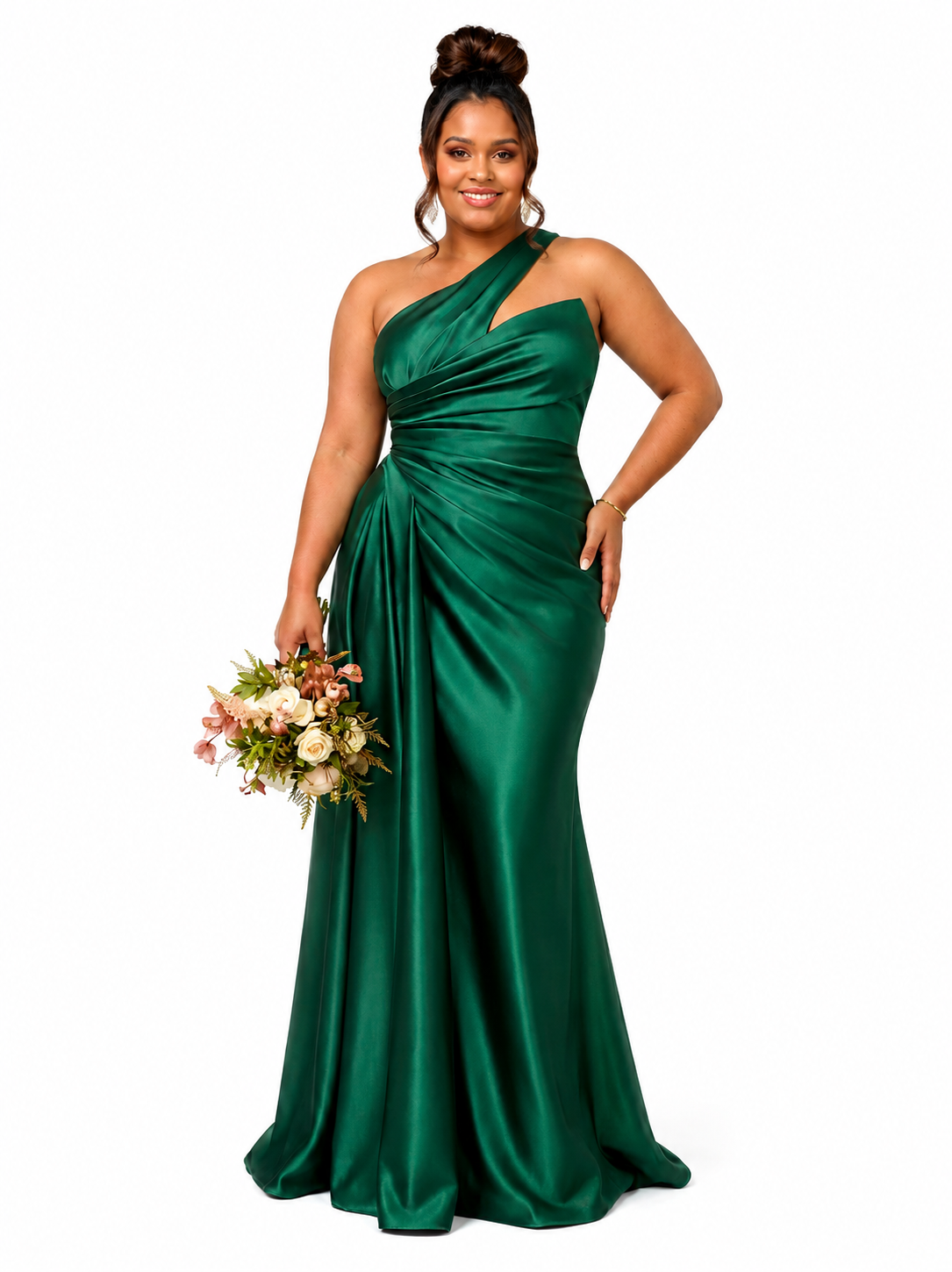 A woman modeling a floor-length emerald green satin one-shoulder gown with a gathered sweetheart neckline and draped skirt, holding a small bouquet of pink and white flowers against a plain white background.