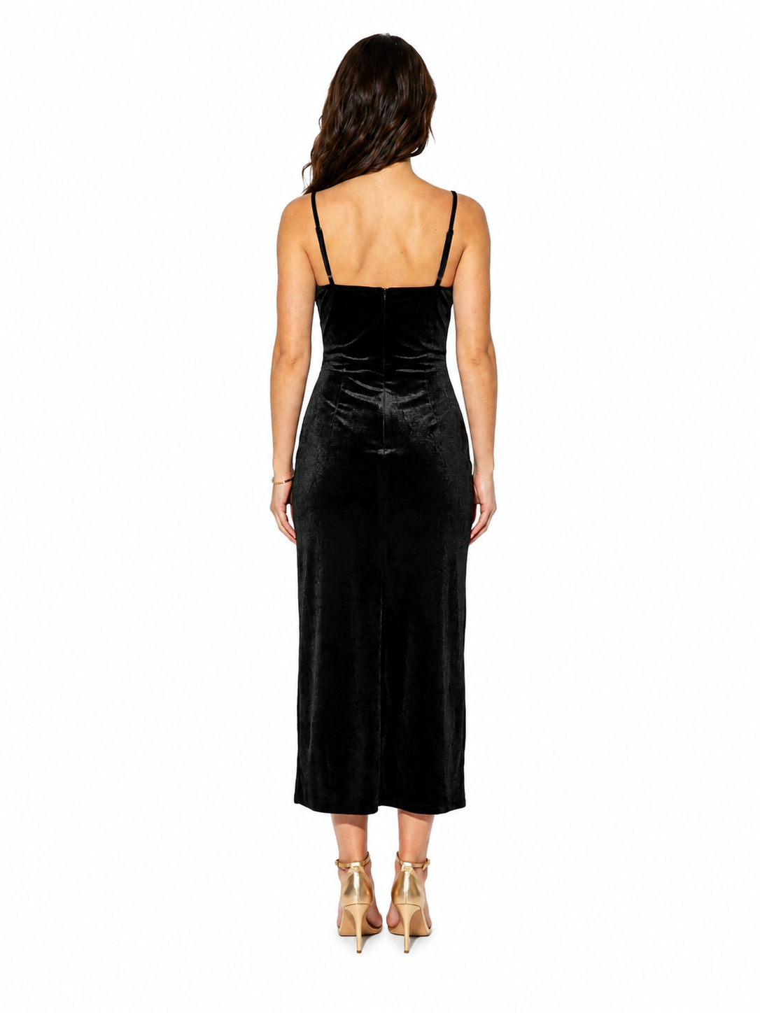 A woman viewed from the back wearing a black velvet spaghetti-strap midi dress and gold high heels against a plain white background.