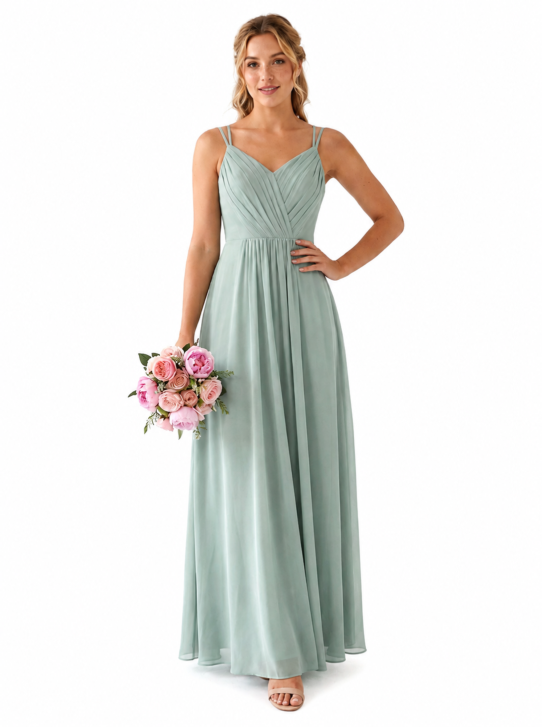 A woman modeling a floor-length sage green bridesmaid dress with thin spaghetti straps and a gathered sweetheart neckline, holding a pink and white flower bouquet against a plain white background.