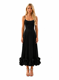 A blonde woman modeling a black spaghetti-strap maxi dress with a flared skirt and ruffled hem, paired with clear high-heeled sandals, against a plain white background.