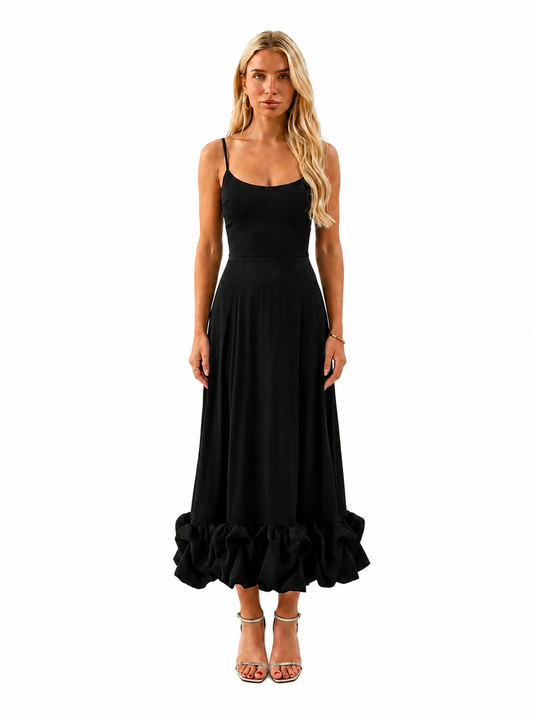 A blonde woman modeling a black spaghetti-strap maxi dress with a flared skirt and ruffled hem, paired with clear high-heeled sandals, against a plain white background.