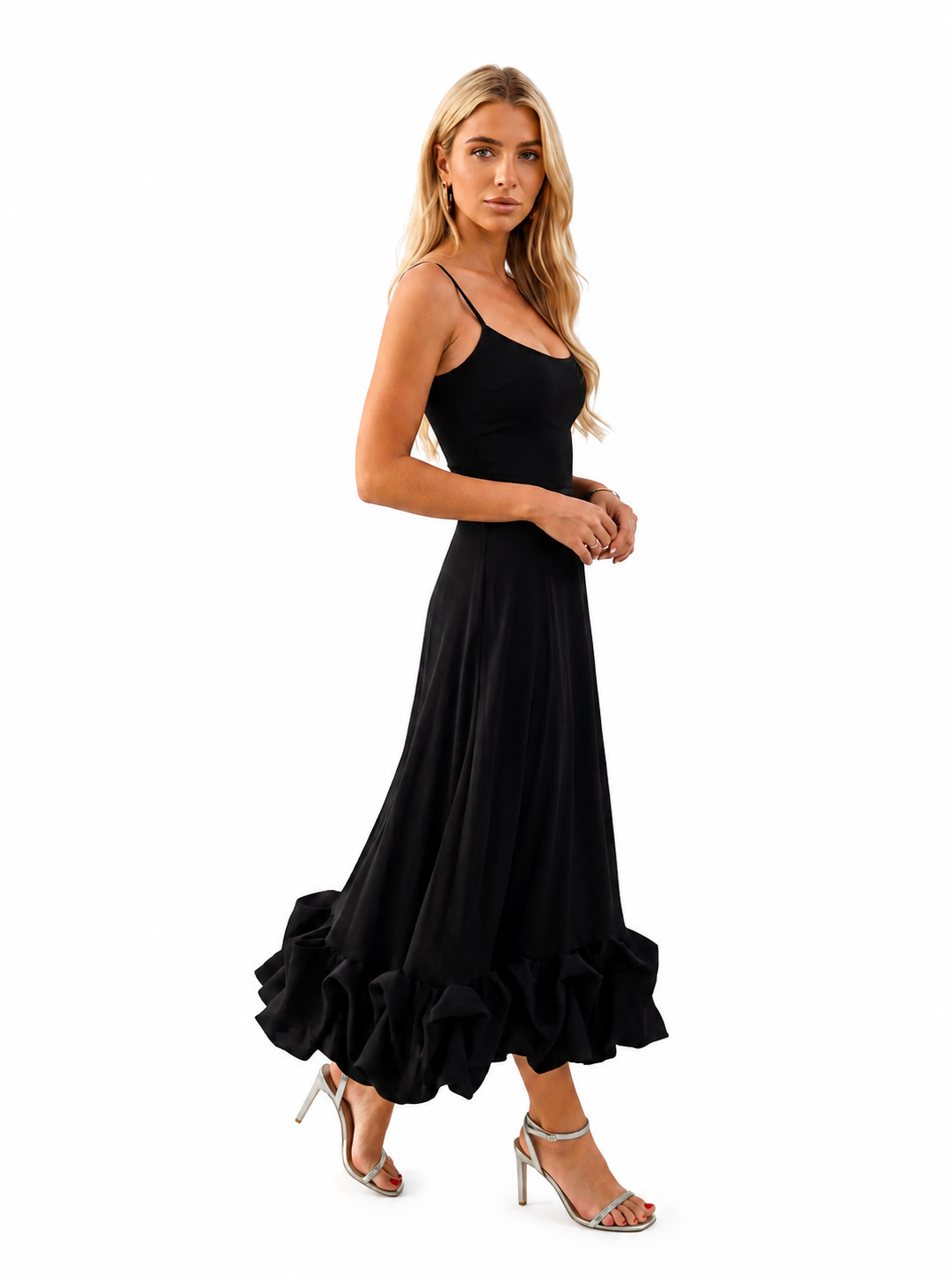 A woman modeling a black maxi dress with spaghetti straps, a fitted bodice, and a voluminous ruffled skirt, paired with silver high-heeled sandals against a plain white background.