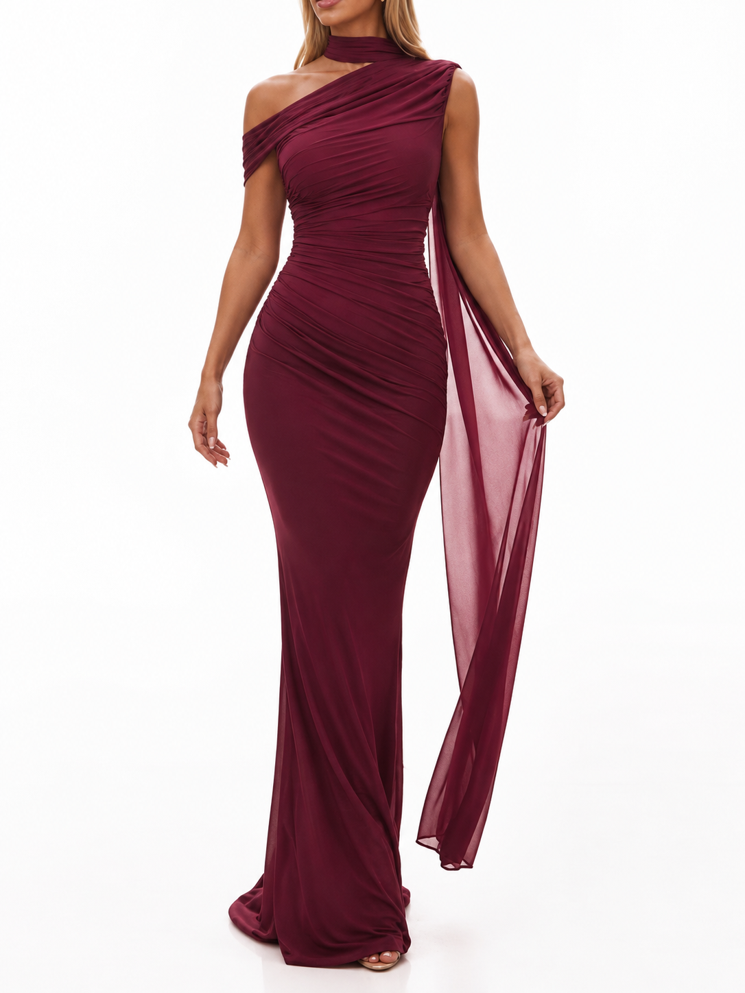 A woman modeling a floor-length, one-shoulder ruched gown in deep burgundy with a matching sheer draped fabric panel, shown against a plain white studio background.